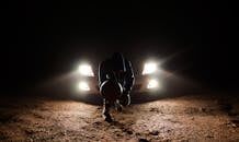 夜晚，汽车前灯照亮了沙地上一名篮球运动员的剪影