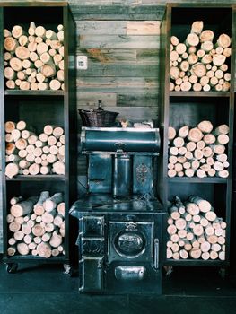 Vintage stove surrounded by shelves of neatly stacked firewood in a rustic indoor setting.