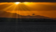 日落时分，一架飞机降落的轮廓引人注目，阳光明媚地洒在海面上