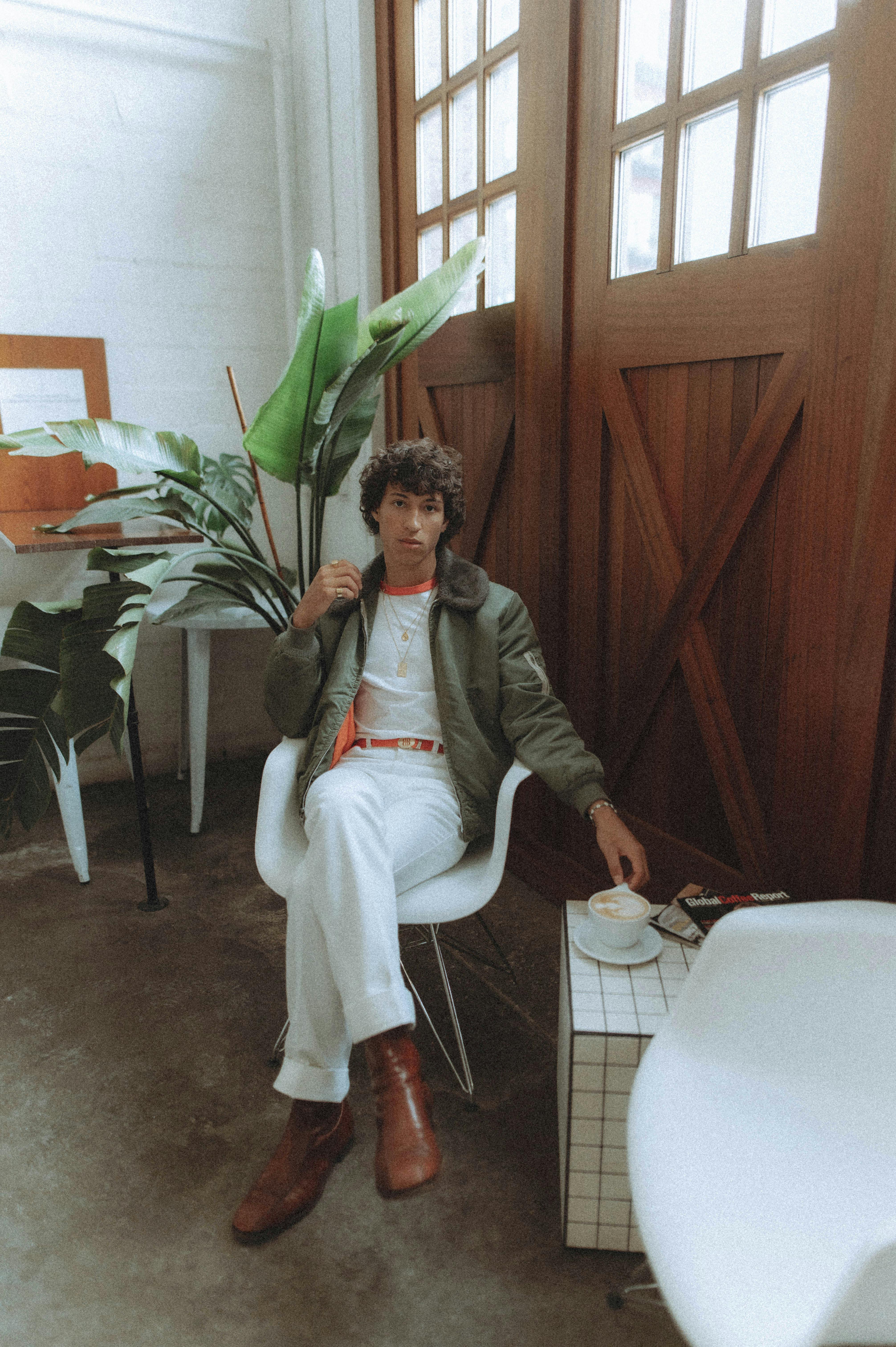 Well-dressed man enjoying a serene moment in a chic café setting with plants.