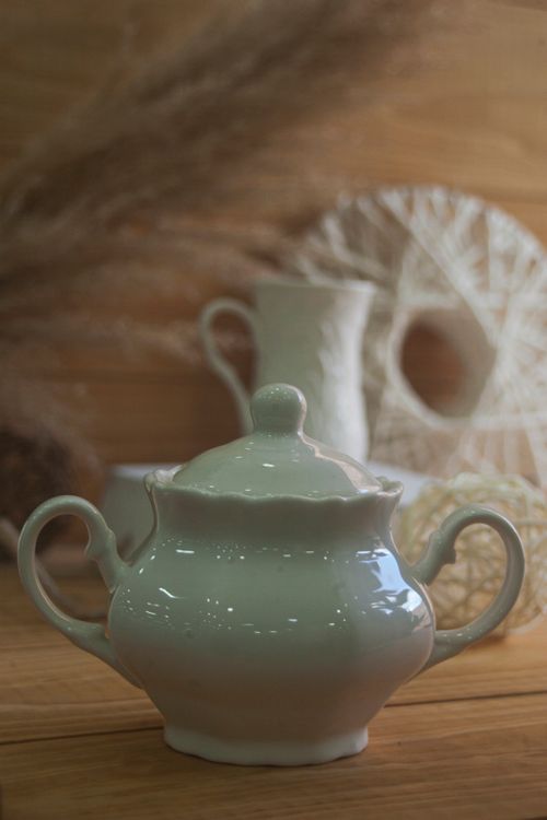 Free Close-up of a ceramic teapot with artistic, woven decorative background on a wooden surface. Stock Photo