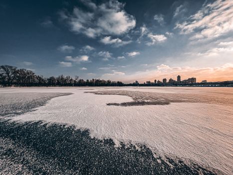 A scenic frozen river view with a city skyline, captured during a winter sunset.