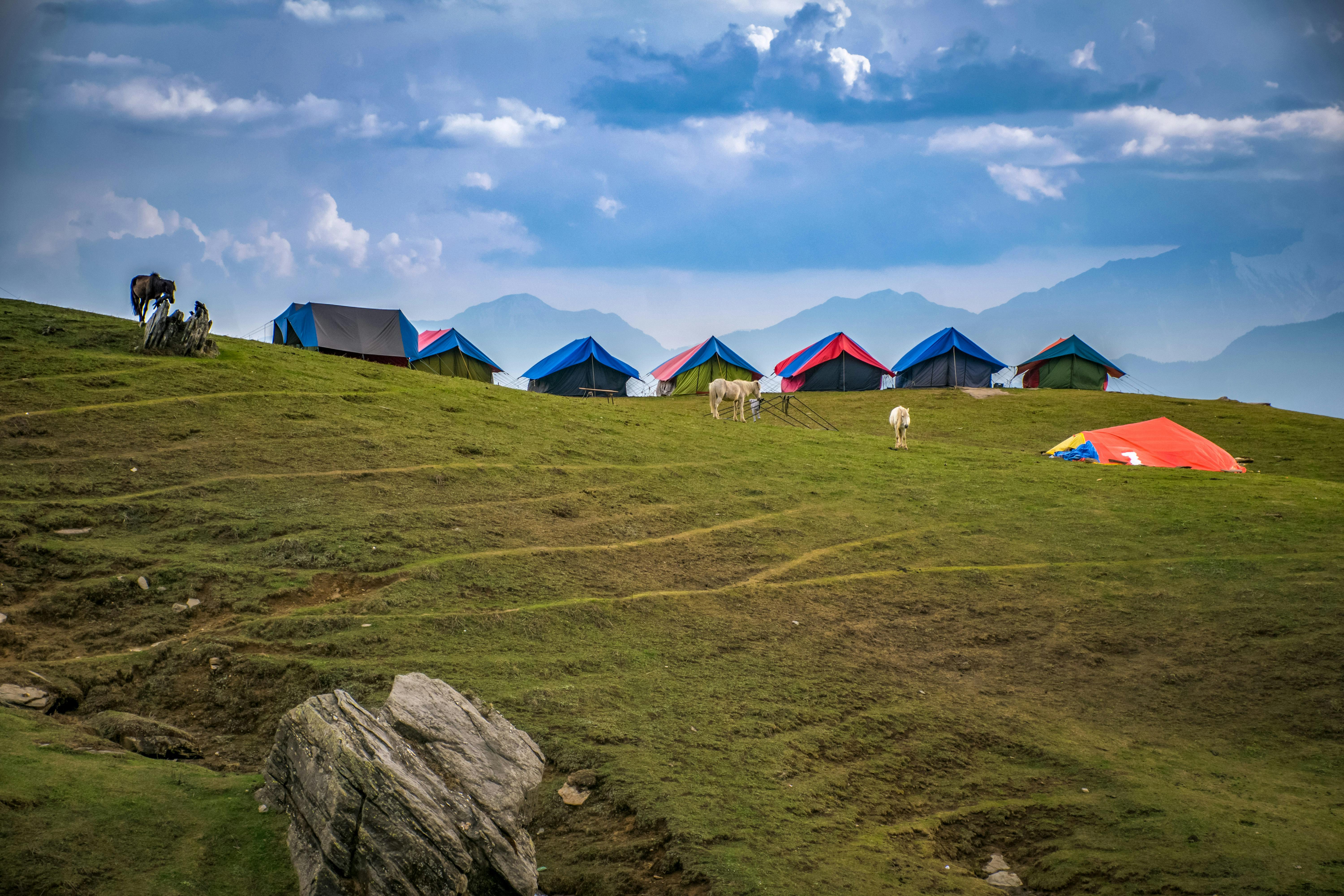 Photographed of Lined Tents on Green Grass Hills · Free Stock Photo