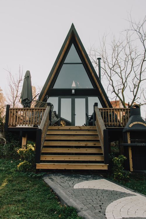 Free A modern A-frame house with a welcoming entrance and wooden steps surrounded by nature. Stock Photo