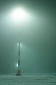 A lighthouse beam piercing through fog on a snowy winter night.