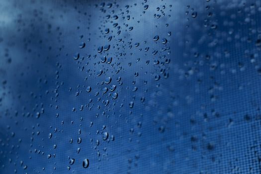 Close-up view of raindrops on a glass window with a blurred blue sky background.