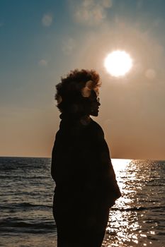 Silhouette of an adult standing by the ocean with a vibrant sunset backdrop.