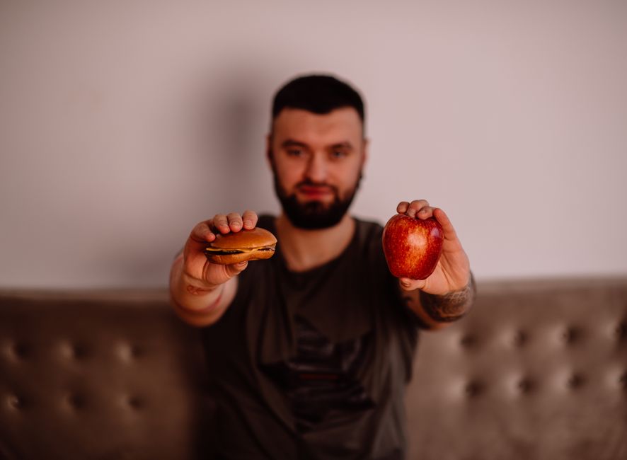 A man holds an apple and a cheeseburger, showcasing a choice between healthy and unhealthy food. A man holds an apple and a cheeseburger, showcasing a choice between healthy and unhealthy food.