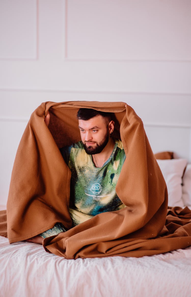 Man Sitting Holding Blanket Over Head