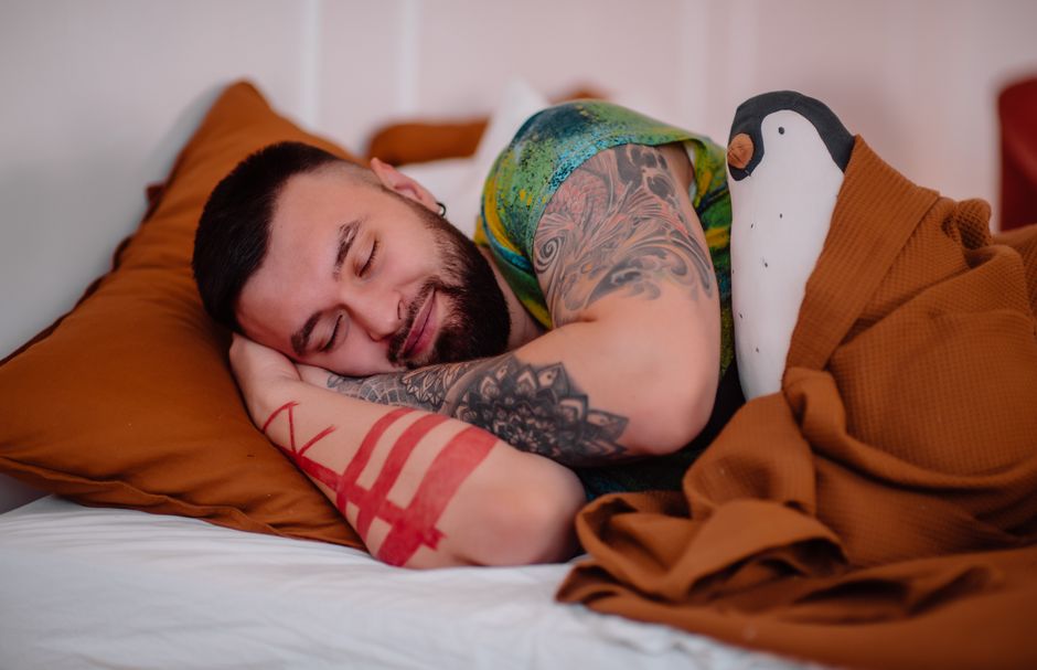A tattooed man with closed eyes sleeps peacefully indoors, showcasing relaxation.