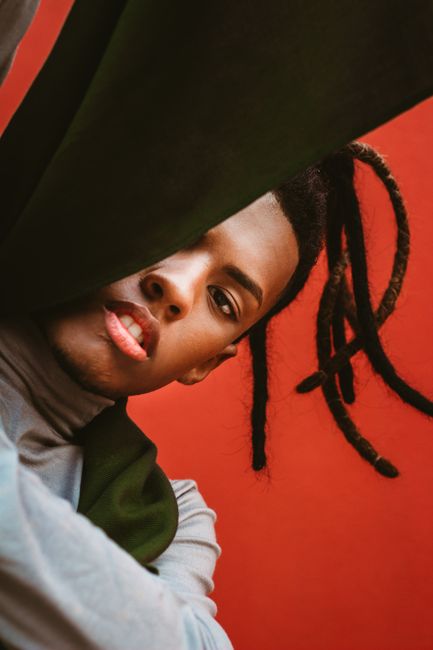Striking low angle portrait of a person with dreadlocks against a bold red background.