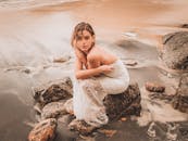 Woman in White Dress Sitting on Rock by the Sea