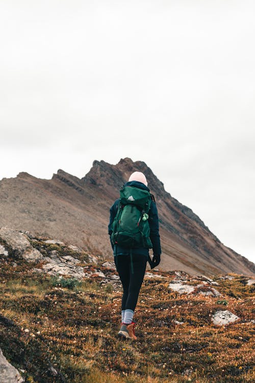 A Person Carrying Green Backpack Walking on Brown Mountain