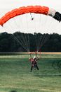 Man in Red Jacket and Black Pants Riding Red and Yellow Parachute
