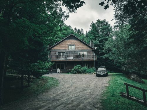 Free Beautiful wooden house nestled in Mont-Tremblant forest with parked car and lush greenery. Stock Photo