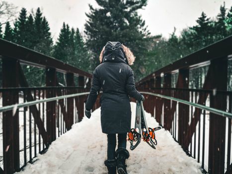 Person walking on snowy bridge in Gatineau, Canada, carrying snowshoes during winter.