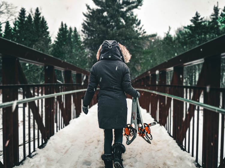 A Back View Of A Person Walking On A Snow Covered Bridge Carrying A Snow Shoes