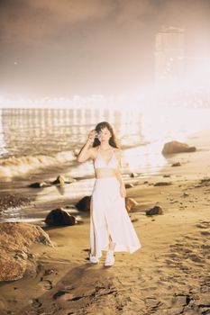 A woman walking along Qui Nhơn beach at night, surrounded by a serene and tranquil seaside setting.