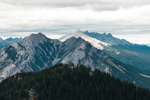 Breathtaking view of the Canadian Rockies with snow-capped peaks and lush forests under a clouded sky.