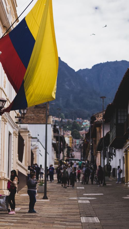 Free Vibrant Colombian flag flutters above a bustling street in Bogotá, capturing urban life. Stock Photo