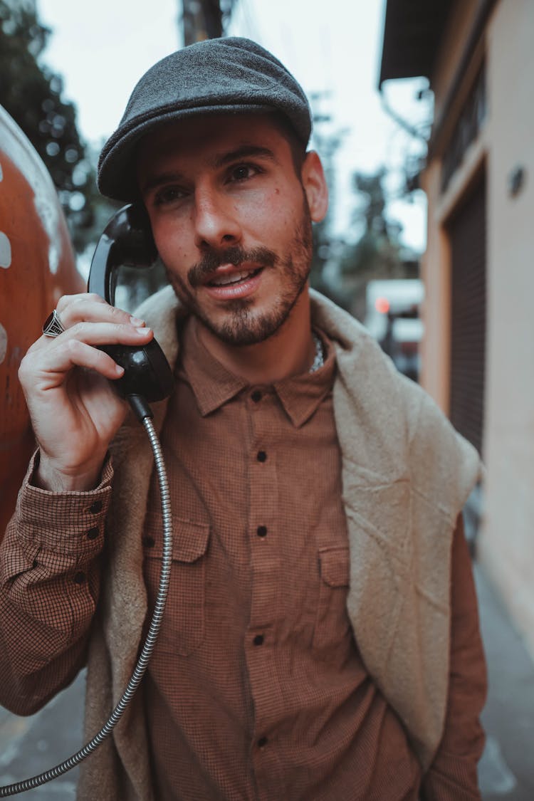 A Man Wearing A Hat Using A Telephone Handset