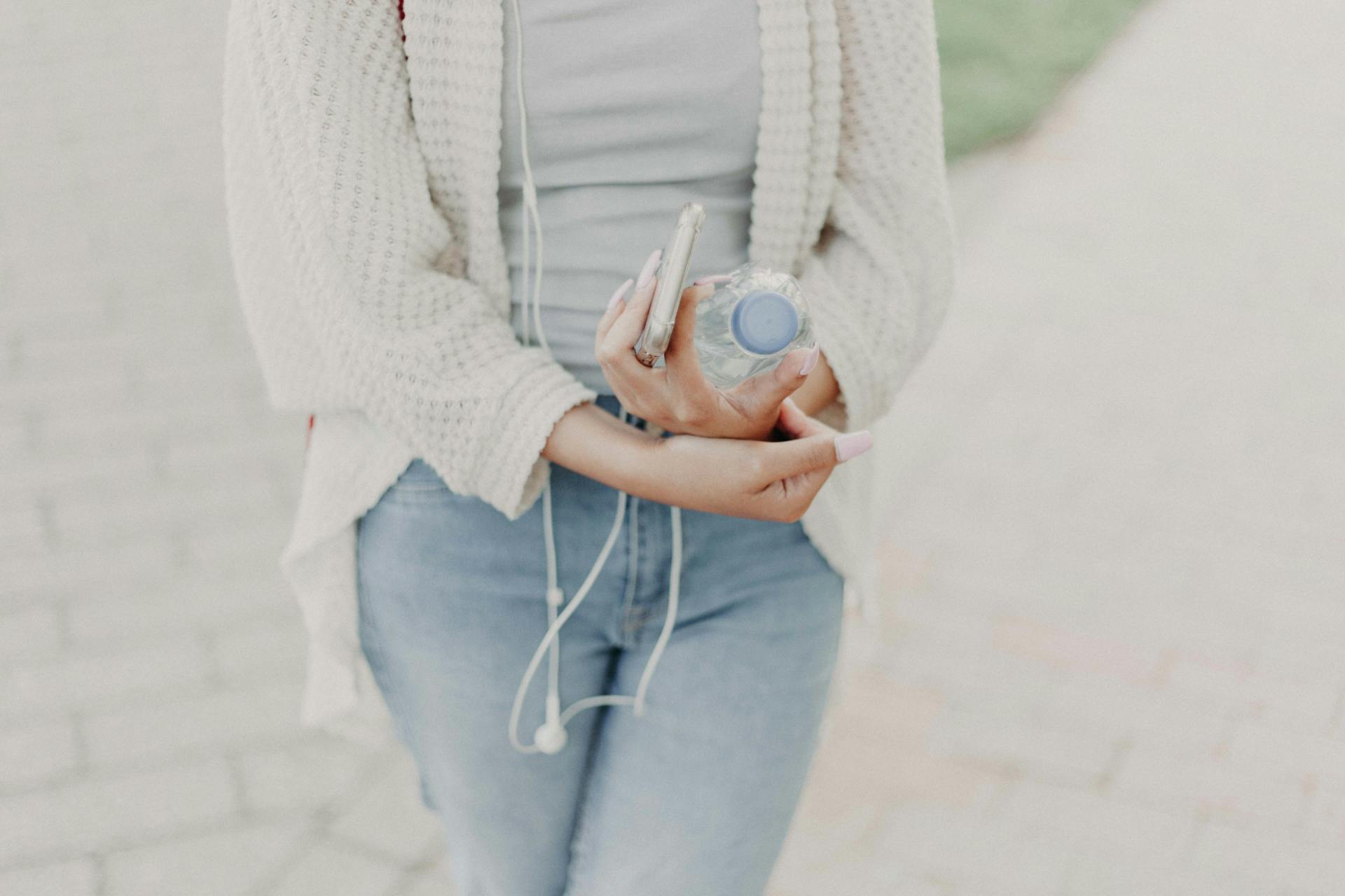 Une femme portant un cardigan blanc et tenant une bouteille en plastique