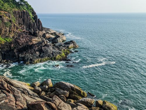 Free Dramatic rocky coastal cliff overlooking a turquoise ocean with waves crashing against the rocks. Stock Photo