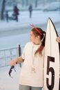 A Woman with Name Tag Holding White Surfboard Under the Snow