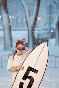A woman in winter attire holding a surfboard, embracing a unique snow-surf theme.