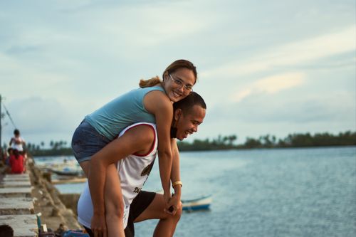 Free Young couple enjoying a playful moment piggyback riding near the water. Stock Photo