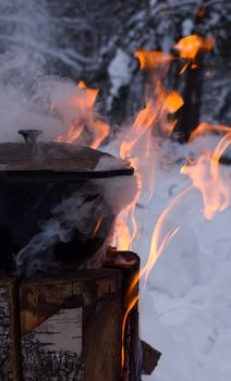A rustic pot over a flame in a snowy winter setting, perfect for outdoor enthusiasts.
