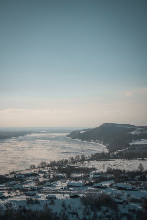 Free A serene aerial view of a seaside village blanketed in snow during winter, with vast frozen sea. Stock Photo