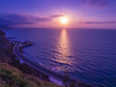 Purple sunrise over the ocean with a view of a winding coastal highway.