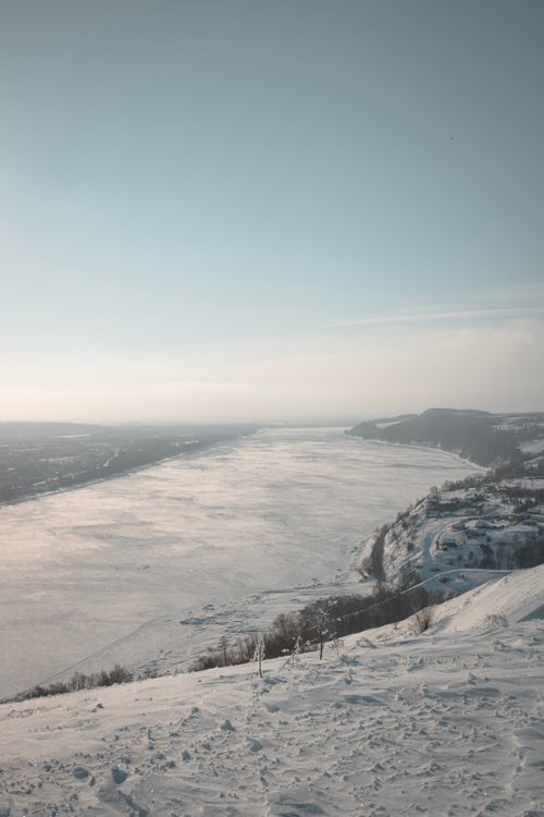 Free A breathtaking winter landscape showcasing a snow-covered river and mountainous terrain under a clear sky. Stock Photo