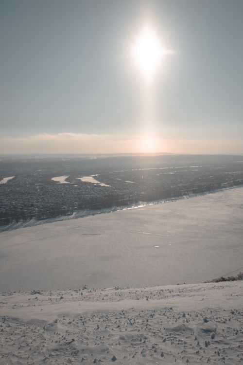 Free A serene winter landscape capturing a frozen river under the bright sun, showcasing vast snow-covered fields. Stock Photo