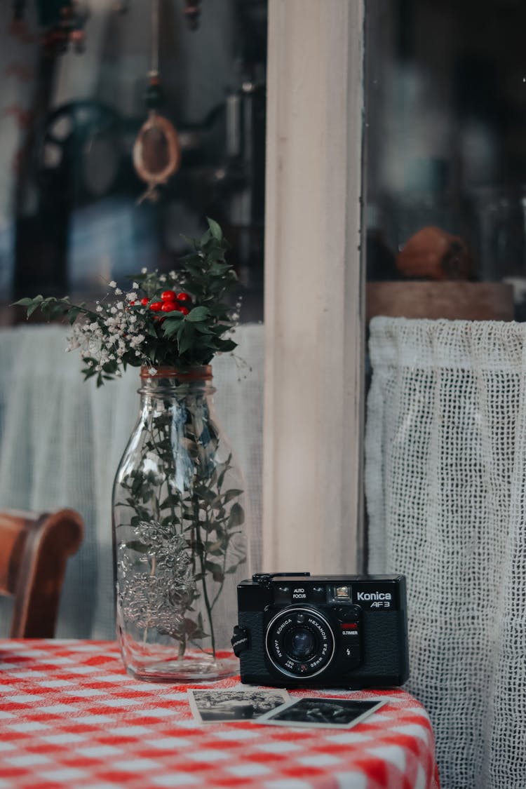 Flowers In Bottle, Camera And Photos On Table