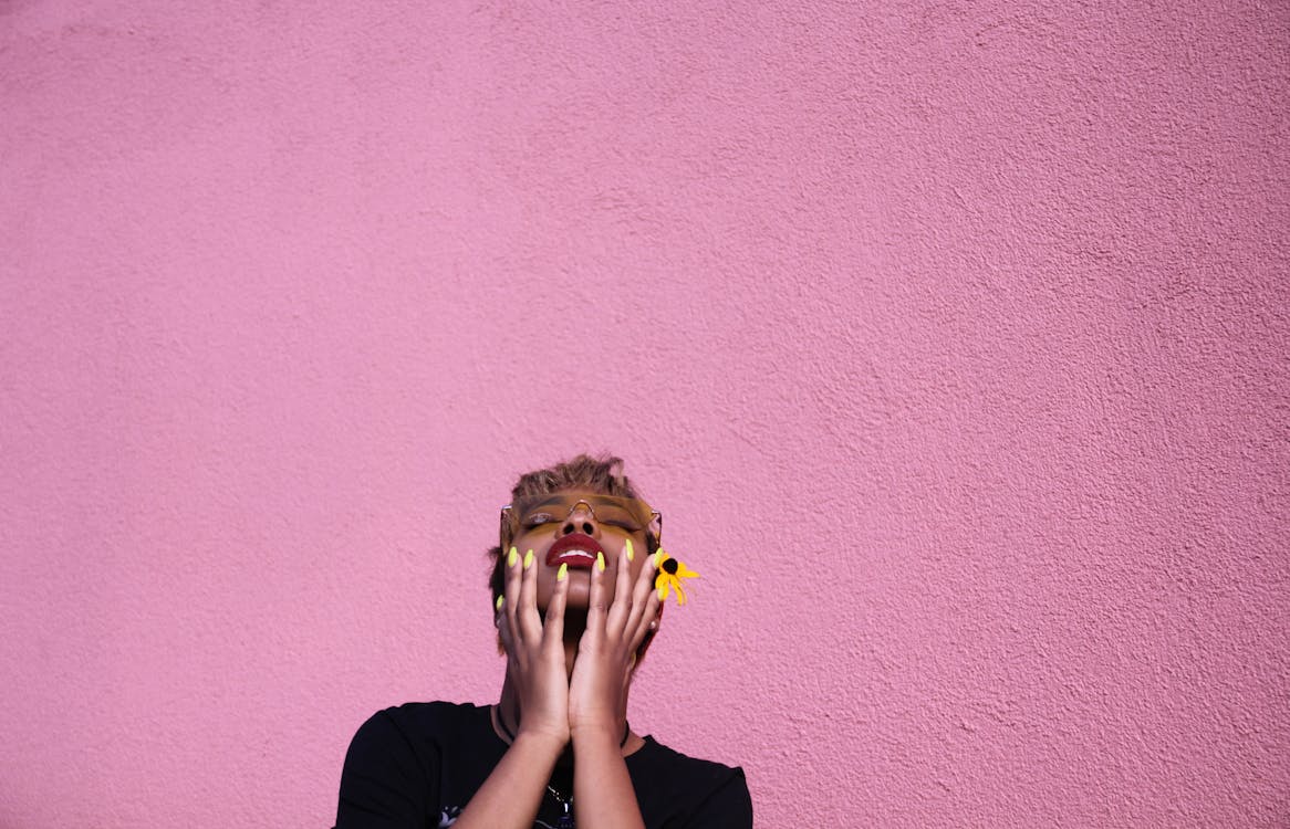 Free Stylish young African American female in casual wear and sunglasses with closed eyes touching face while throwing head back on pink background Stock Photo