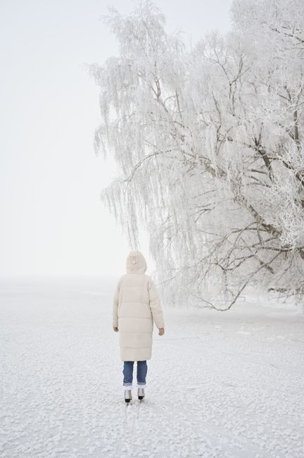 Person ice skating on a frozen lake surrounded by snow-covered trees in winter.