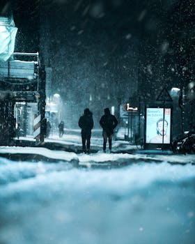 Wintry street scene in Lübeck, Germany, depicting snowfall and people walking under city lights.