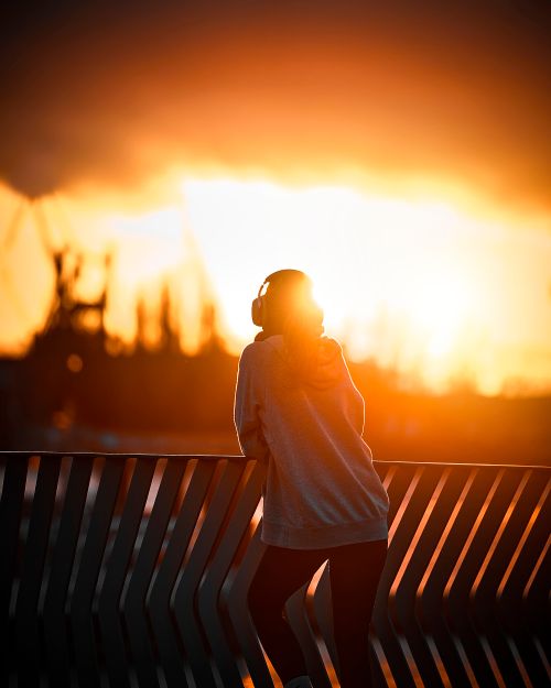Free Silhouette of a person with headphones overlooking a vibrant sunset, creating a serene urban scene. Stock Photo