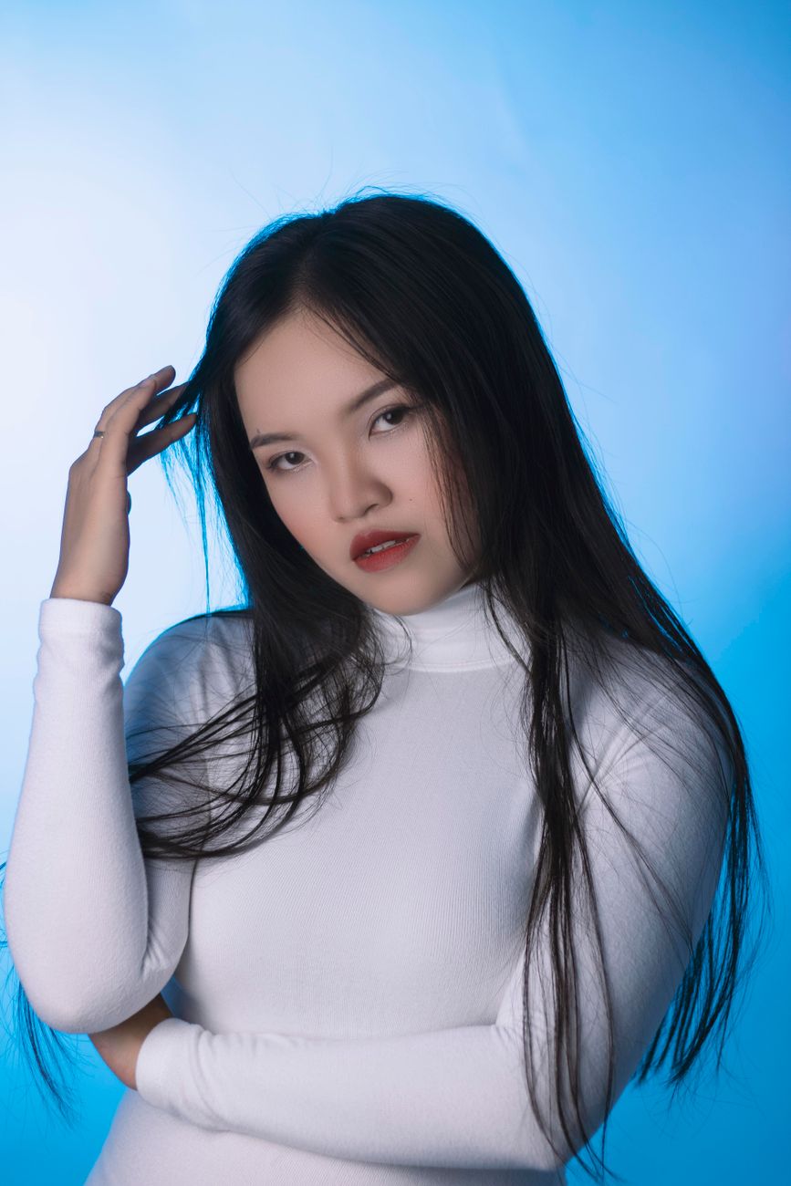 Fashion portrait of a woman in a white turtleneck against a blue background.