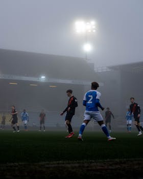 Dramatic evening soccer match under spotlights in Peterborough, England with players engaged in action.