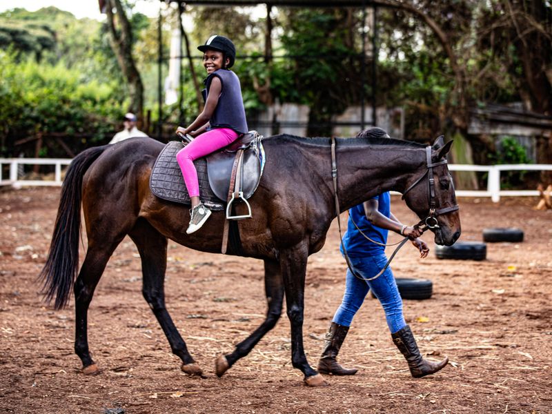 Smiling young rider in a helmet on a horse led by a guide in a paddock