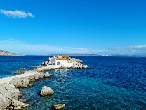 Free A picturesque white chapel on a rocky island surrounded by clear blue sea in Sikiada. Stock Photo