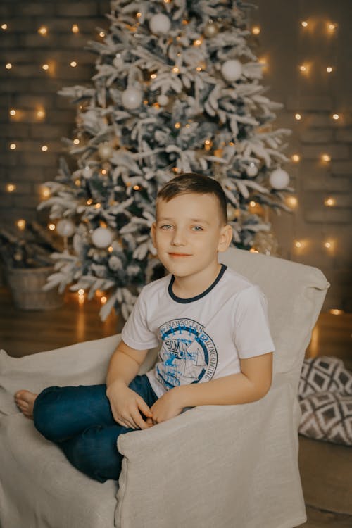 Boy Sitting in Armchair in front of Christmas Tree