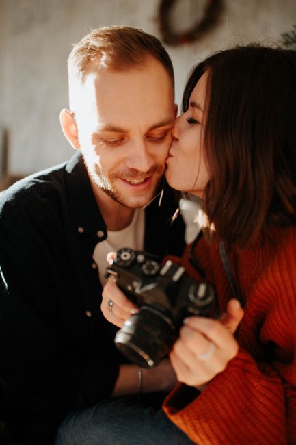 A woman kisses her partner while holding a vintage camera, sharing a romantic moment.