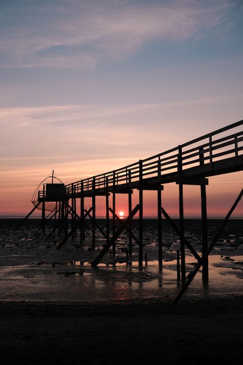 Free Silhouette of a pier at sunset in Les Moutiers-en-Retz, capturing the serene coastal beauty. Stock Photo