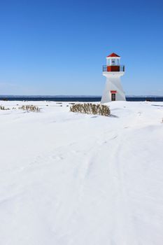 Lighthouse standing in a snow-covered landscape under a blue sky, Quebec.