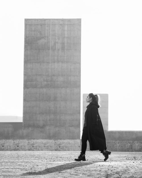 Free Black and white portrait of a woman walking near large concrete structures. Stock Photo