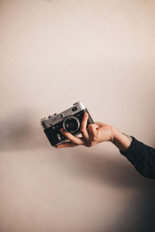 Free A person holds a vintage camera against a neutral background, ideal for creative projects. Stock Photo